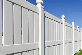 A white vinyl privacy fence with decorative pointed post caps, stretching into the distance against a clear blue sky.