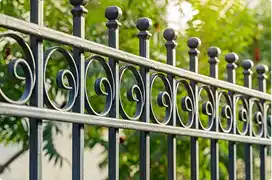 A close-up of an ornamental black wrought iron fence with a scroll pattern and ball-topped finials.